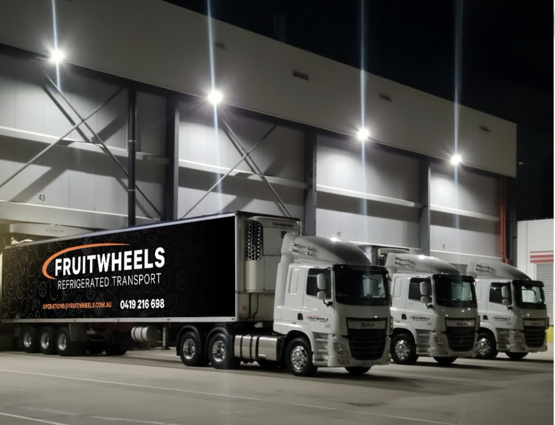 Three Fruit Wheels prime movers lined up on the distribution centre docks at night